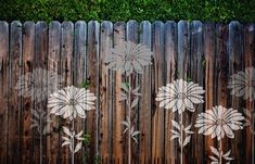 a wooden fence with white flowers painted on the wood and grass in front of it