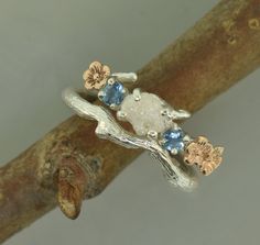 a silver ring with blue and white stones on it's side sitting on top of a tree branch