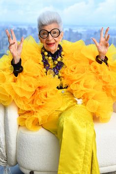 an older woman sitting in a chair with her hands up and wearing yellow dress on the couch