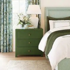 a bedroom with green and white bedding, two nightstands and a lamp on top of the night stand