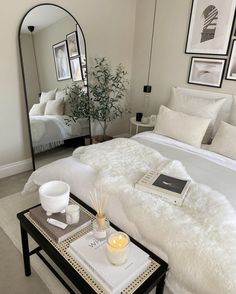 a white bed sitting in a bedroom next to a table with a mirror on it