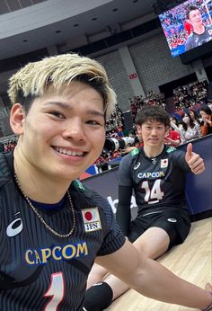 two young men sitting on the floor at a basketball game