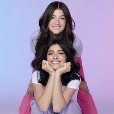 two young women sitting on top of each other with their arms around one another and smiling at the camera