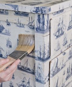 a person holding a paintbrush in front of a painted dresser with blue and white wallpaper