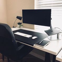 a desk with a computer monitor, keyboard and mouse on it in front of a window