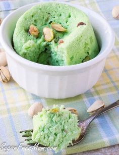 a bowl filled with green cake and nuts on top of a table next to a spoon