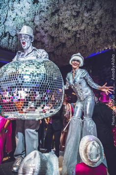 two people dressed in silver dancing around a disco ball