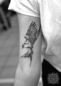 a black and white photo of a person with a bird tattoo on their left arm