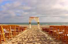 an outdoor wedding setup on the beach with wooden chairs and white drapes draped over them