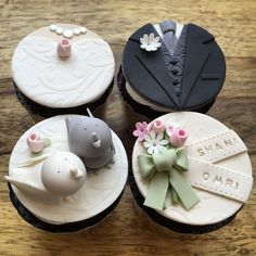 four cupcakes decorated with fondant decorations on top of a wooden table,