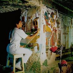 a woman sitting on top of a chair next to a wall covered in egyptian paintings