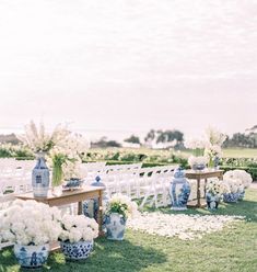 an outdoor ceremony setup with white flowers and blue vases on the grass near chairs