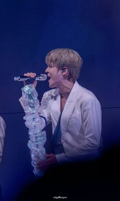 a man in white shirt and tie holding a microphone up to his mouth while standing on stage