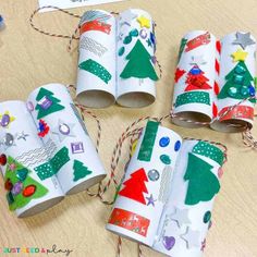 four rolls of toilet paper decorated with christmas trees and decorations, tied in twine