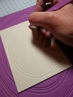 a person cutting out paper on top of a purple mat with a pair of scissors