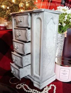 a white jewelry cabinet sitting on top of a red blanket next to a christmas tree