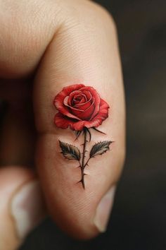 a small red rose tattoo on the middle finger and thumbnail, with leaves around it