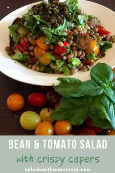 bean and tomato salad with crispy capers on a white plate surrounded by fresh basil leaves