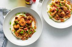 two white bowls filled with shrimp and grits next to silverware on a table