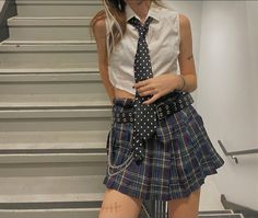 a woman wearing a skirt and tie standing in front of stairs with her hands on her hips