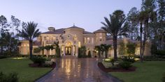 a large house with lots of palm trees in the front yard and driveway leading to it