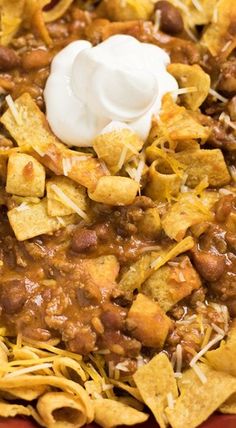 chili and cheese nachos with sour cream in a red casserole dish