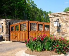 a gated entrance to a home with flowers in the foreground and trees in the background