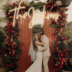 a bride and groom kissing in front of a neon sign