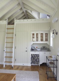 a kitchen with white walls and wooden stairs leading up to the upper floor, next to a ladder