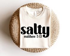 a white t - shirt with the word salty printed on it sitting next to a wicker basket