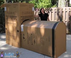 a woman is sitting in a cardboard mailbox on the sidewalk and waving her hand