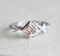 an engagement ring with a pink diamond and three white diamonds on the side, sitting on top of a piece of cloth