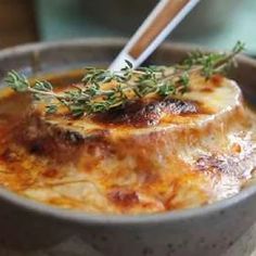 a close up of a bowl of food with a spoon in it and some herbs on top