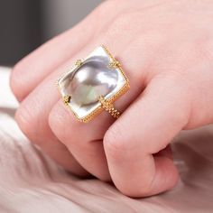 This natural Mabe Pearl is in the shape of a square. It seems to burst out of its golden frame, giving it a 3D quality. We highlighted the natural beauty of this one-of-a-kind gemstone by encasing it in a handmade, 18k gold bezel.Ready to ship in size 7. Please allow 1-2 weeks for any other size. Technical Details Metal: 18k yellow goldMabe Pearl: 18.42 cts.Ring face: 22 x 22mmBand width: 2mmHandmade in New YorkStyle # R-2467-MP Luxury Yellow Gold Pearl Ring With Cabochon, Polished Cushion Cut Yellow Gold Jewelry, Yellow Gold Cabochon Pearl Ring For Gift, Yellow Gold Cabochon Pearl Ring As Gift, Luxury Gold Pearl Ring With High Luster, Luxury Jewelry With Polished Finish And Rectangular Stone, Luxury Jewelry With Polished Rectangular Stone, Gold Rectangular Jewelry With Bezel Setting, Cabochon Pearl Ring In Yellow Gold For Gift