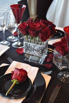 a table set with red roses in vases and place settings for two people to sit at