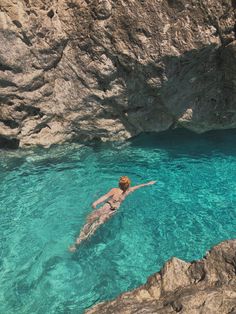 a woman swimming in clear blue water next to rocks