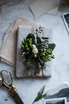 a table topped with flowers and greenery on top of a white cloth next to scissors