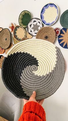 a person holding up several woven baskets in front of a wall with different designs on it