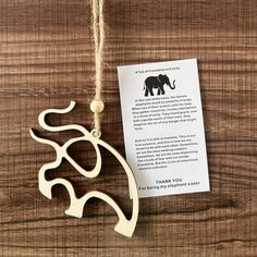 an elephant ornament hanging from a string on a wooden table with a note attached to it