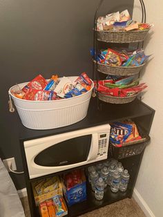 a microwave oven sitting on top of a black shelf filled with snacks and drinks in baskets