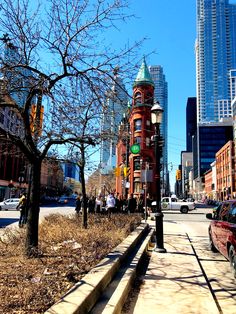 a city street with tall buildings in the background and cars parked on the side of the road