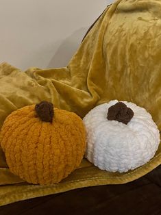 two knit pumpkins are sitting on a yellow velvet blanket, one is white and the other is brown