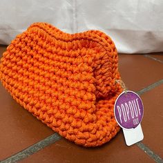 an orange crocheted bag with a tag on it sitting on a tile floor