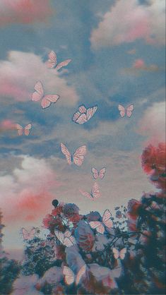 there are many pink butterflies flying in the sky above some bushes and trees with red flowers on them