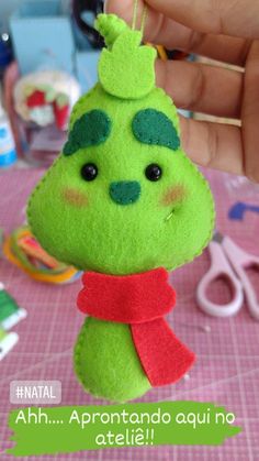 a hand holding a green stuffed animal on top of a pink cloth covered table next to scissors and other crafting supplies