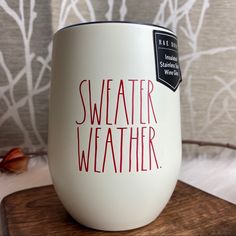 a white coffee cup with the words sweater weather on it sitting on top of a wooden board