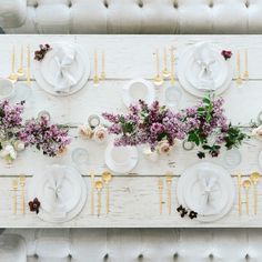 the table is set with white plates and purple flowers