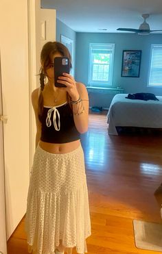 a woman taking a selfie while wearing a white skirt and black top in a bedroom