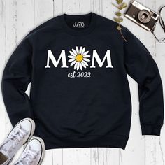 Celebrate the beauty of motherhood with our exclusive Daisy Mom Est collection - a perfect blend of comfort, style, and sentimental charm. Our Daisy Mom Est Sweatshirt is more than just apparel; it's a floral masterpiece that captures the essence of motherly love and devotion. Elevate your Mother's Day style with our Mothers Day Long Sleeve Shirt, a tasteful tribute to the extraordinary women who shape our lives. Embrace the floral elegance with our Floral Mama Sweatshirt, a cozy yet chic piece Casual Mother's Day Sweatshirt For Family, Casual Sweatshirt For Mother's Day Family Event, Casual Sweatshirt For Mother's Day Family Gathering, Casual Sweatshirt For Mother's Day, Casual Sweatshirt For Family Mother's Day, Casual Black Sweatshirt For Mother's Day, Mother's Day Black Graphic Print Sweatshirt, Black Graphic Print Mother's Day Sweatshirt, Family Matching Sweatshirt For Mother's Day