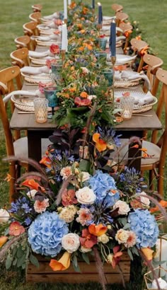 a long table set up with blue and orange flowers, candles and plates on it